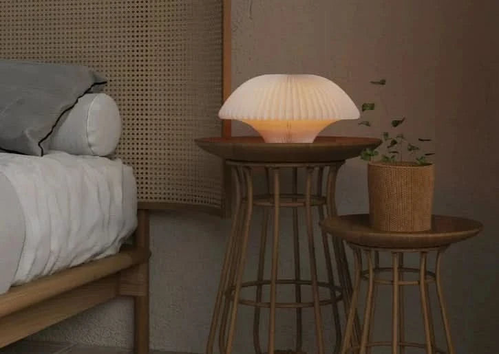 White pleated origami bell-shaped paper bedside lamp on a wooden table in a bedroom.